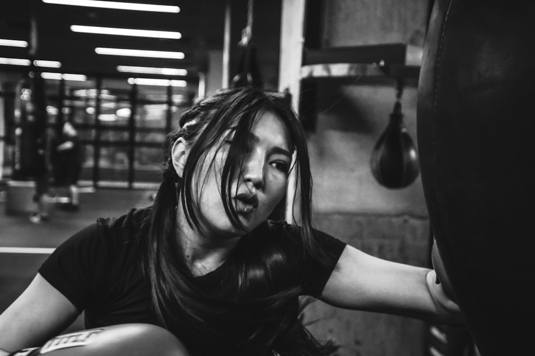 A woman sitting on a punching bag in a gym, An Asian woman boxing