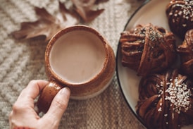 A person holding a cup of coffee next to a plate of cookies