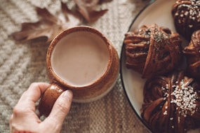 A person holding a cup of coffee next to a plate of cookies