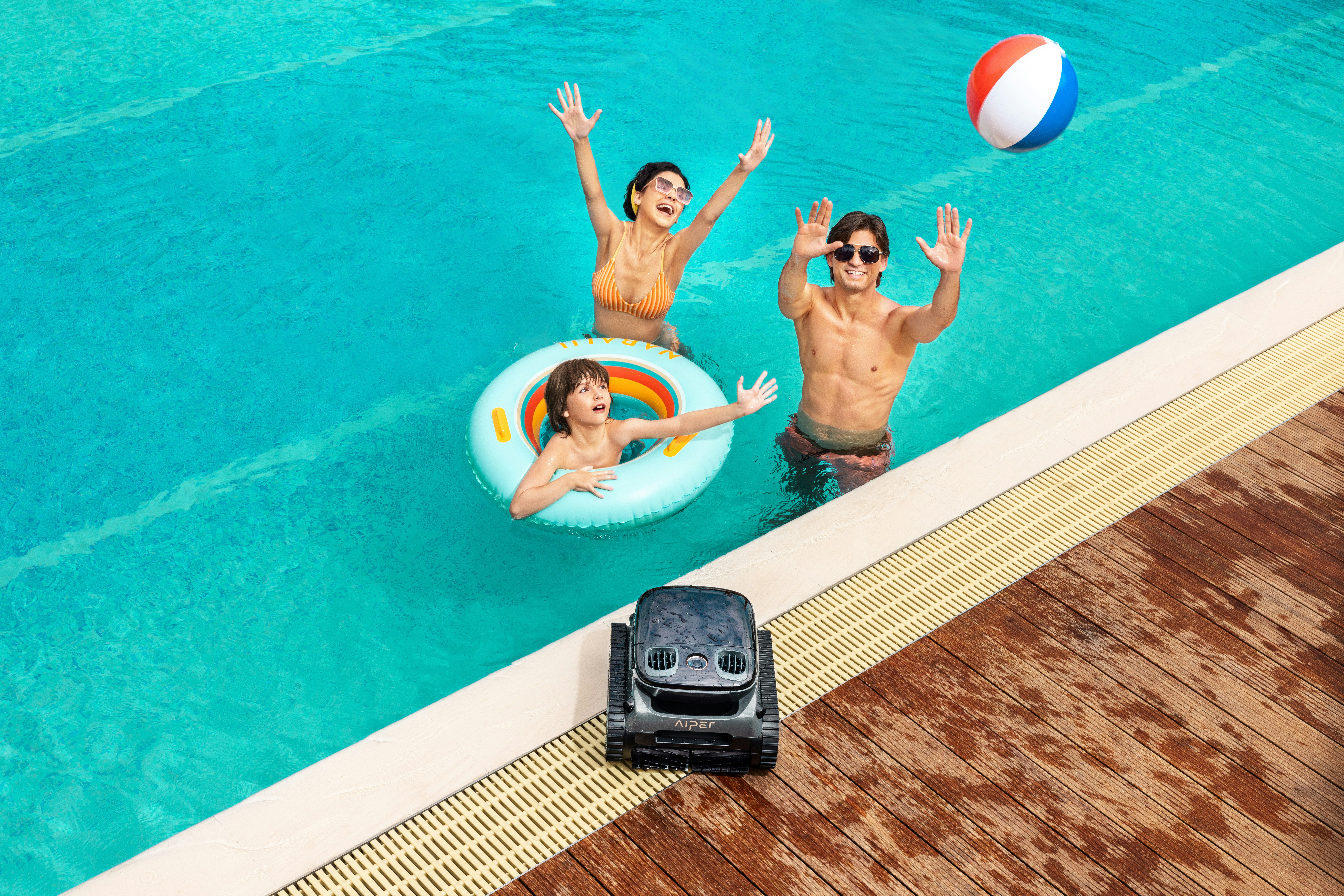 A family enjoying pool time with a beach ball, while Aiper robotic pool cleaner sits at the poolside, ready for action.