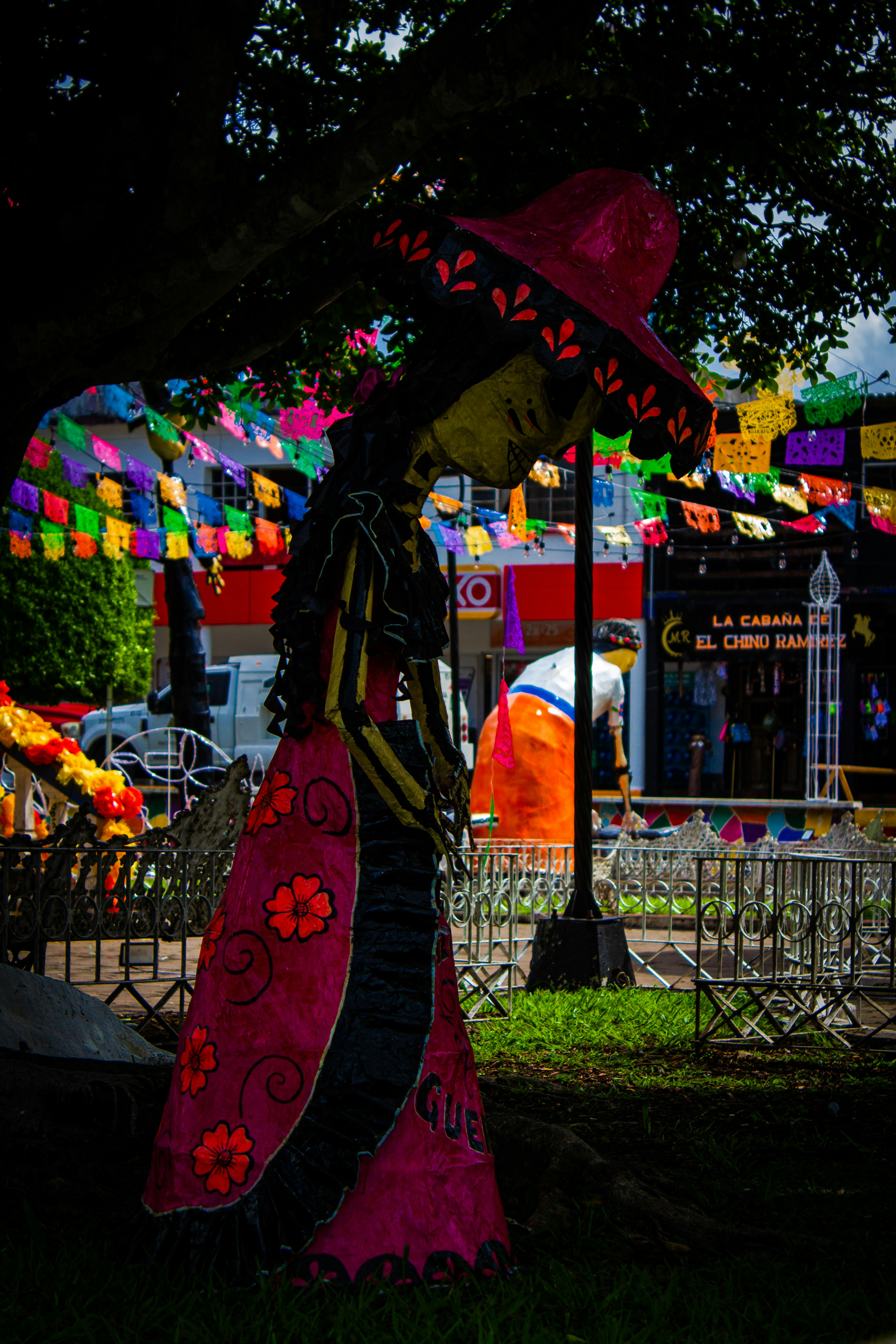 A woman in a colorful dress and hat standing under a tree