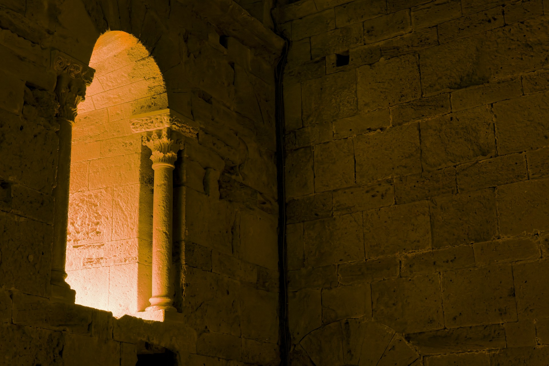 A light shines through a window in a stone building