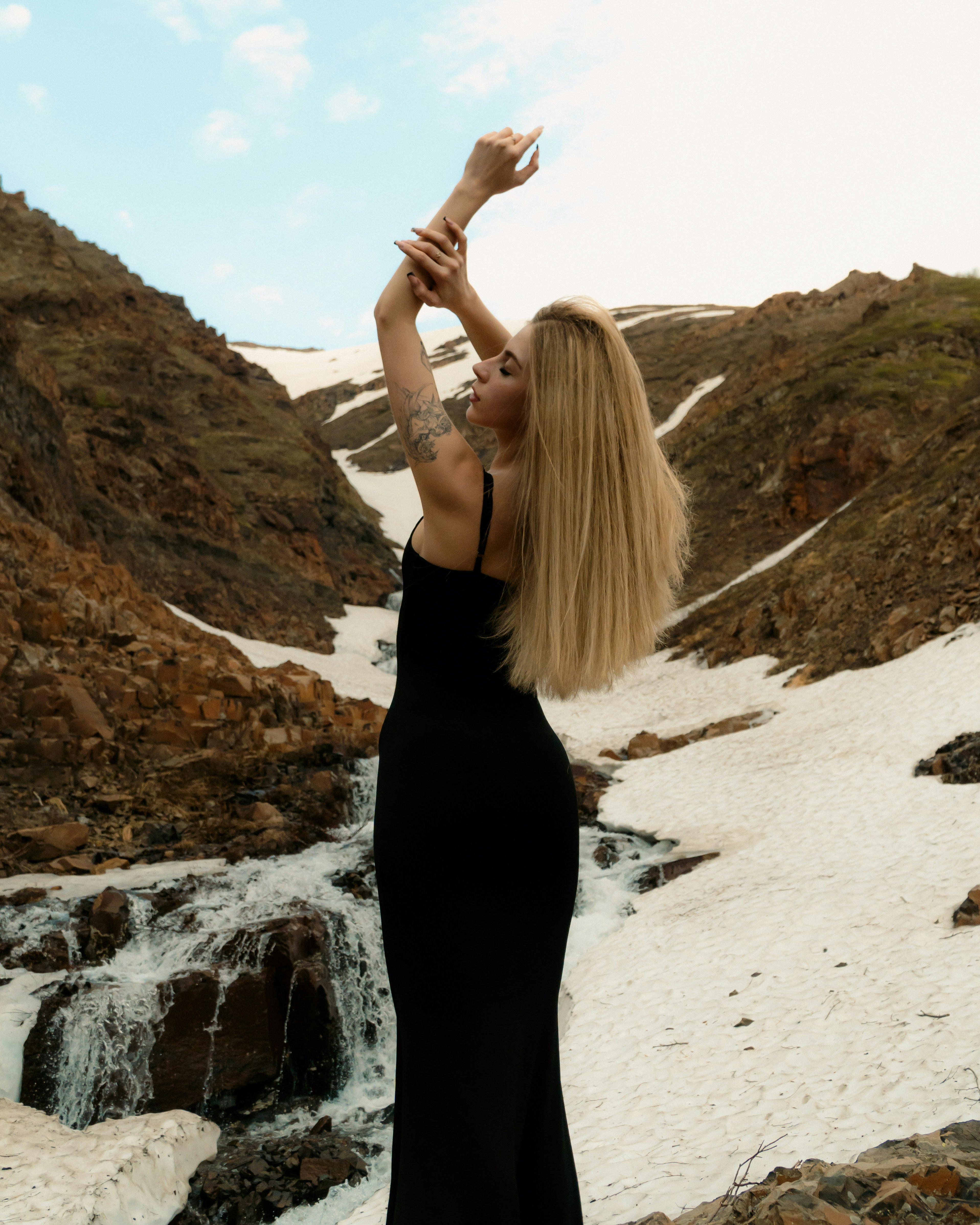 A woman in a black dress standing in front of a waterfall