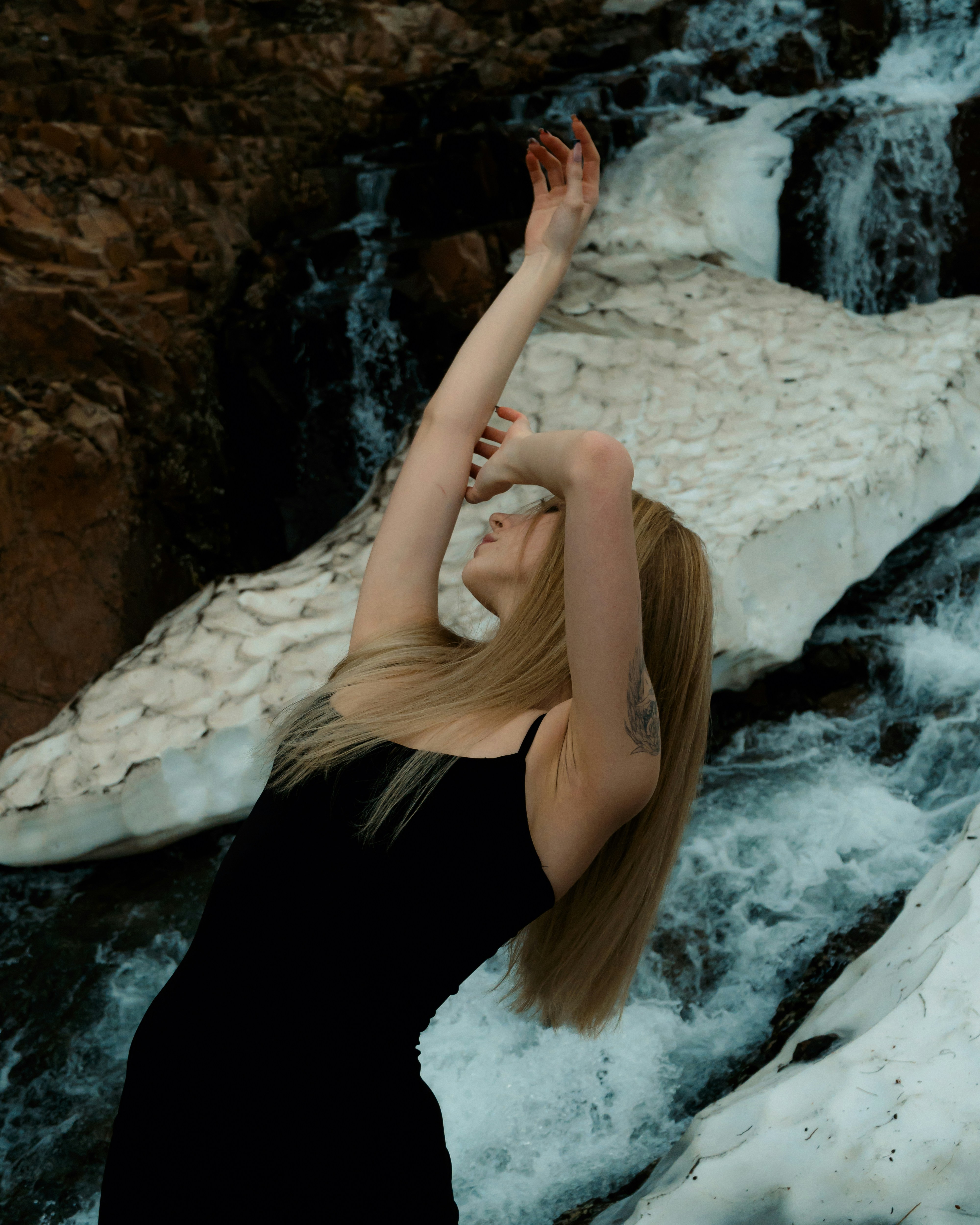 A woman in a black dress standing in front of a waterfall