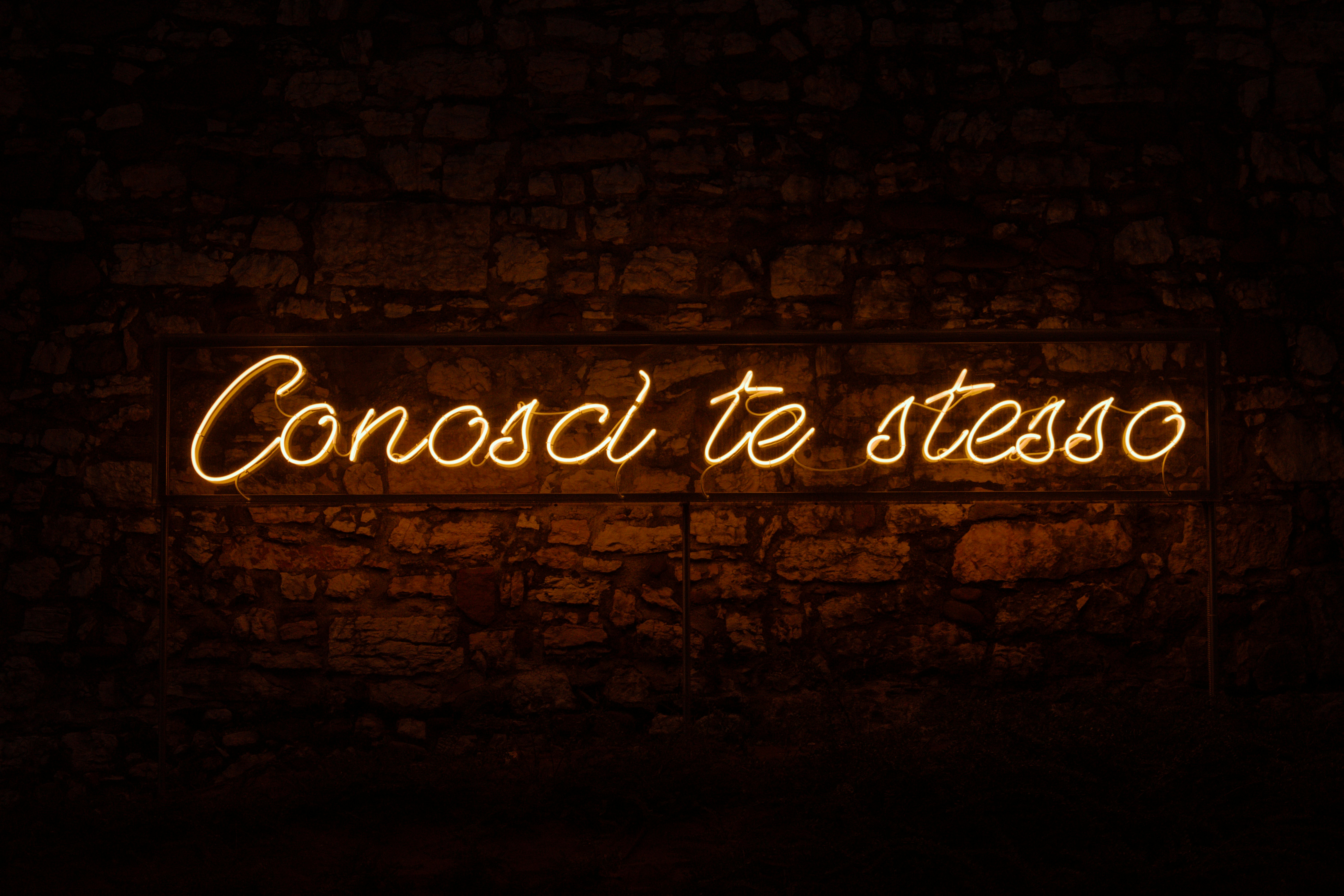 A brick wall with a neon sign that reads conoci te steso