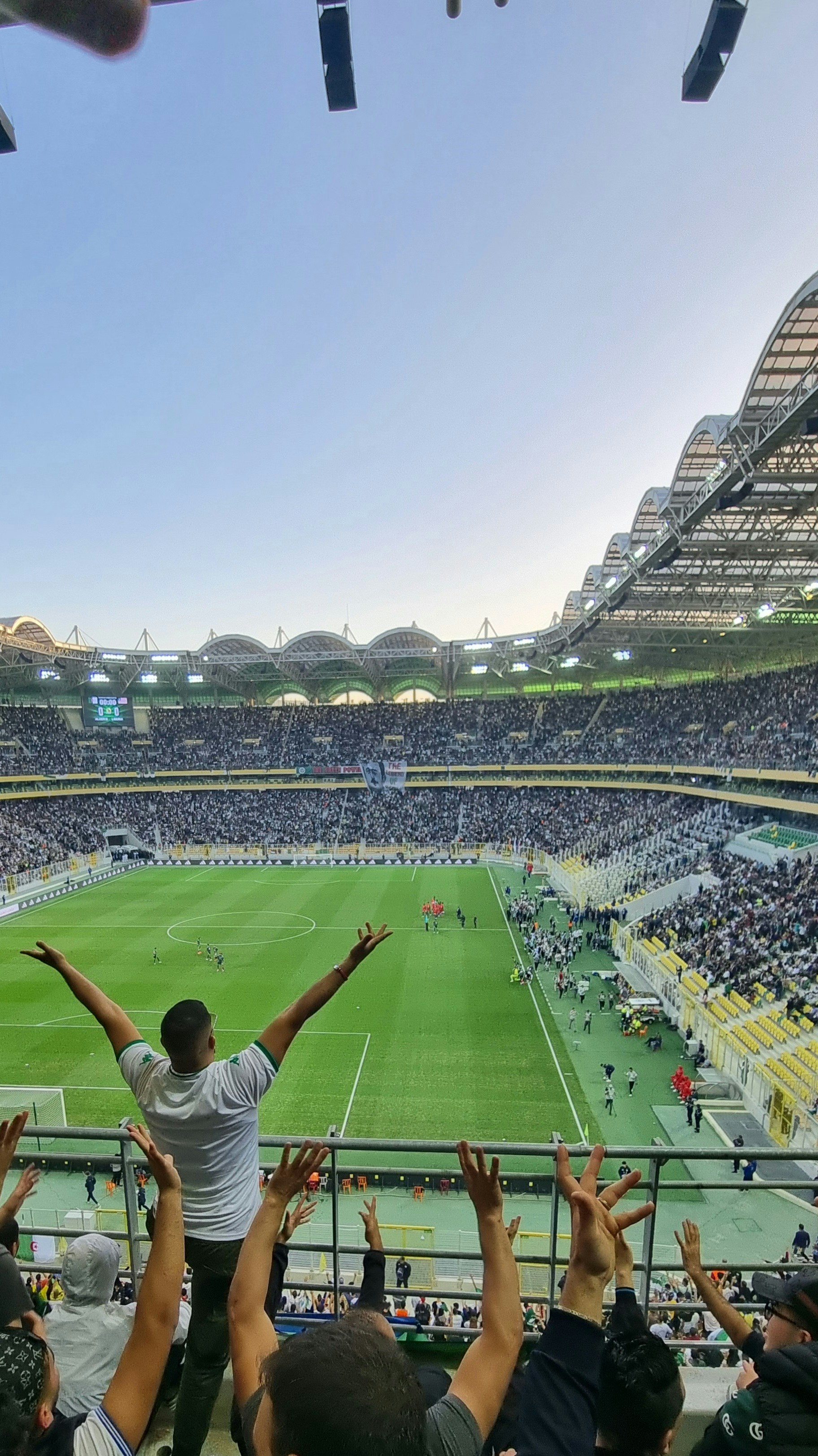 Football crowd celebrating a goal, raised arms, dark stadium atmosphere, electric energy