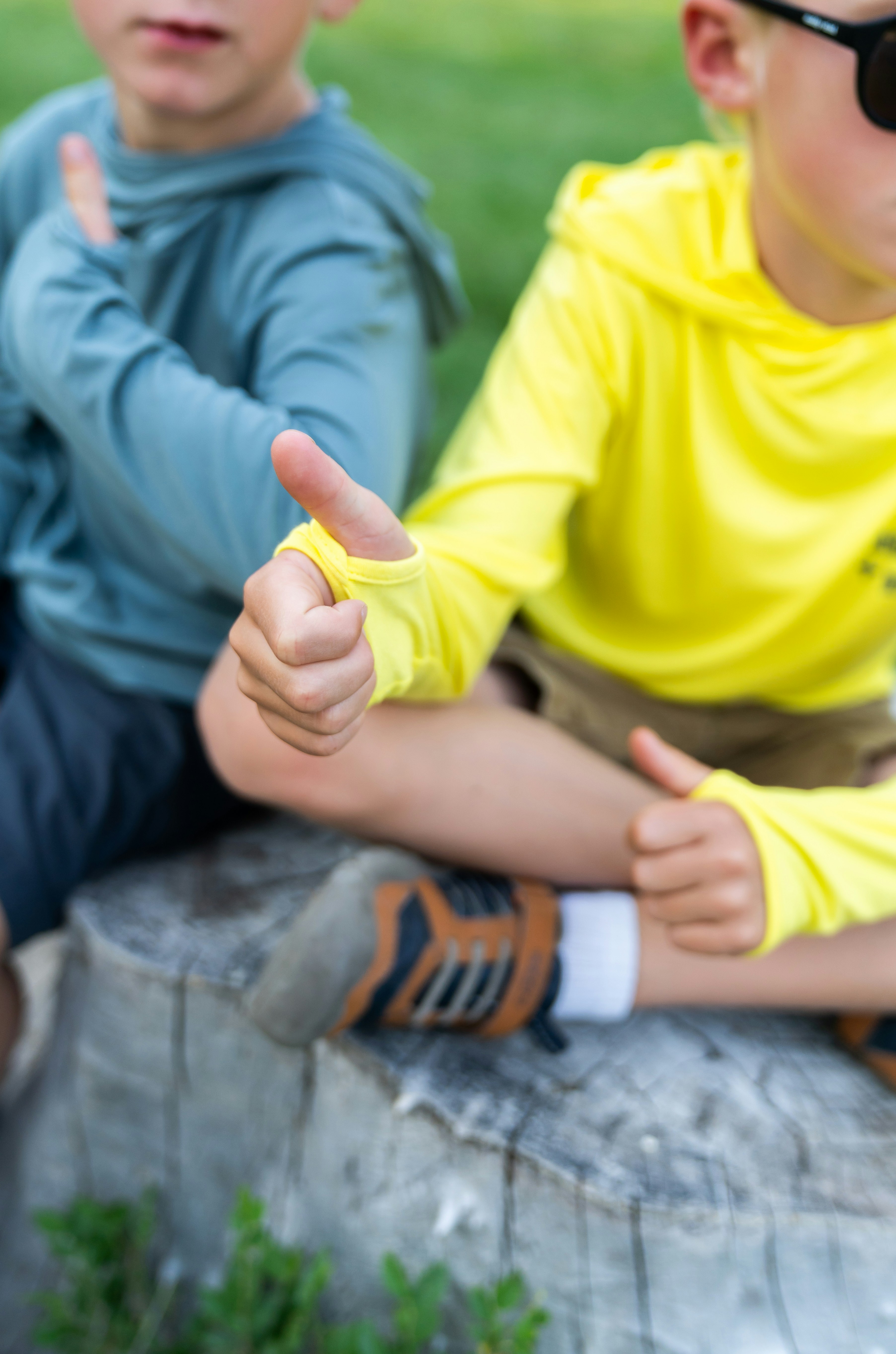 Two young boys sitting on a rock giving thumbs up