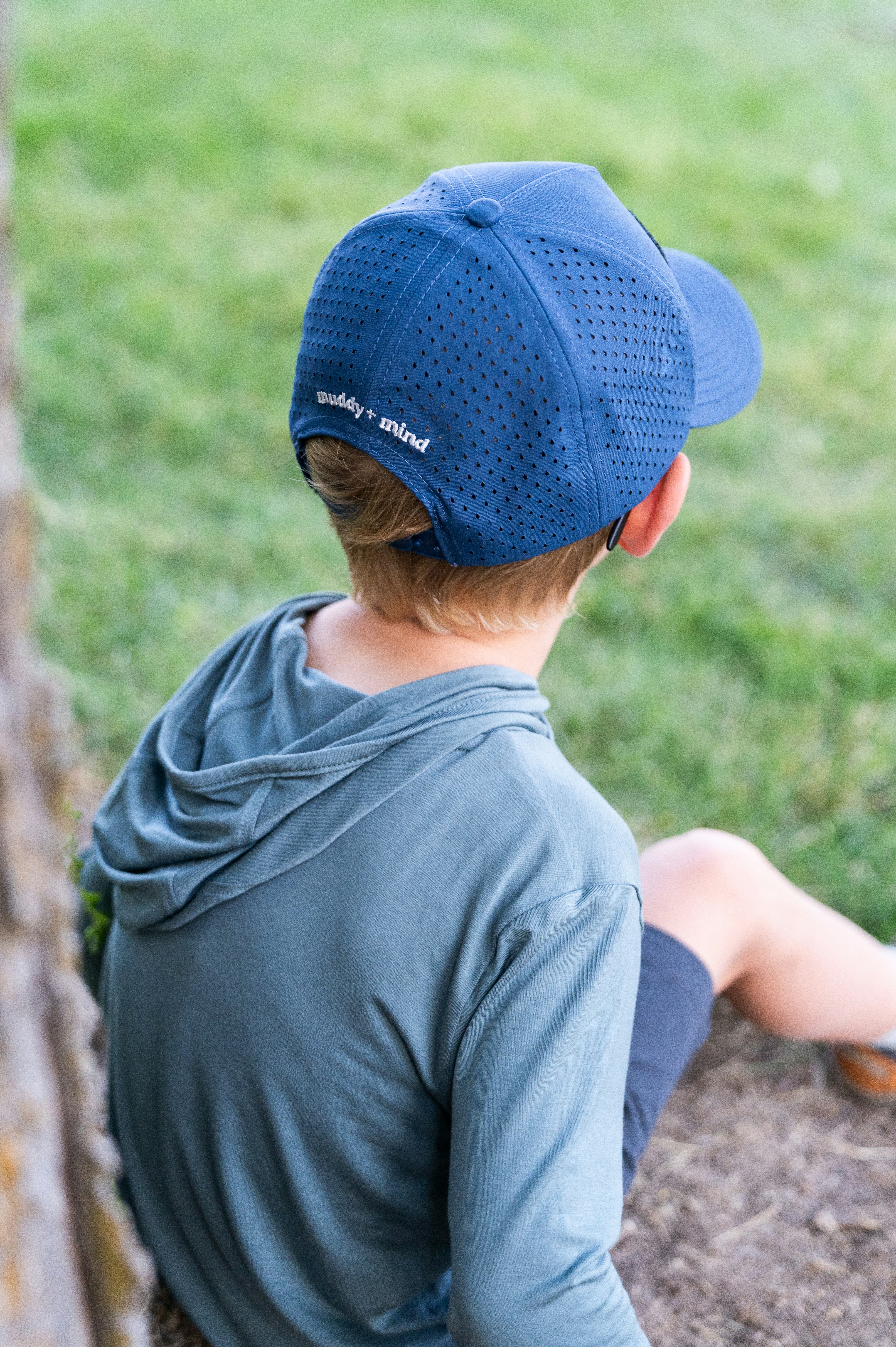 A young boy sitting on the ground next to a tree