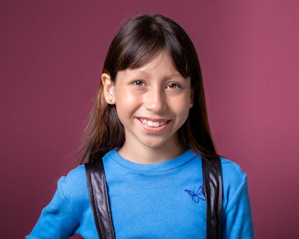 A young girl wearing a blue shirt and a black backpack