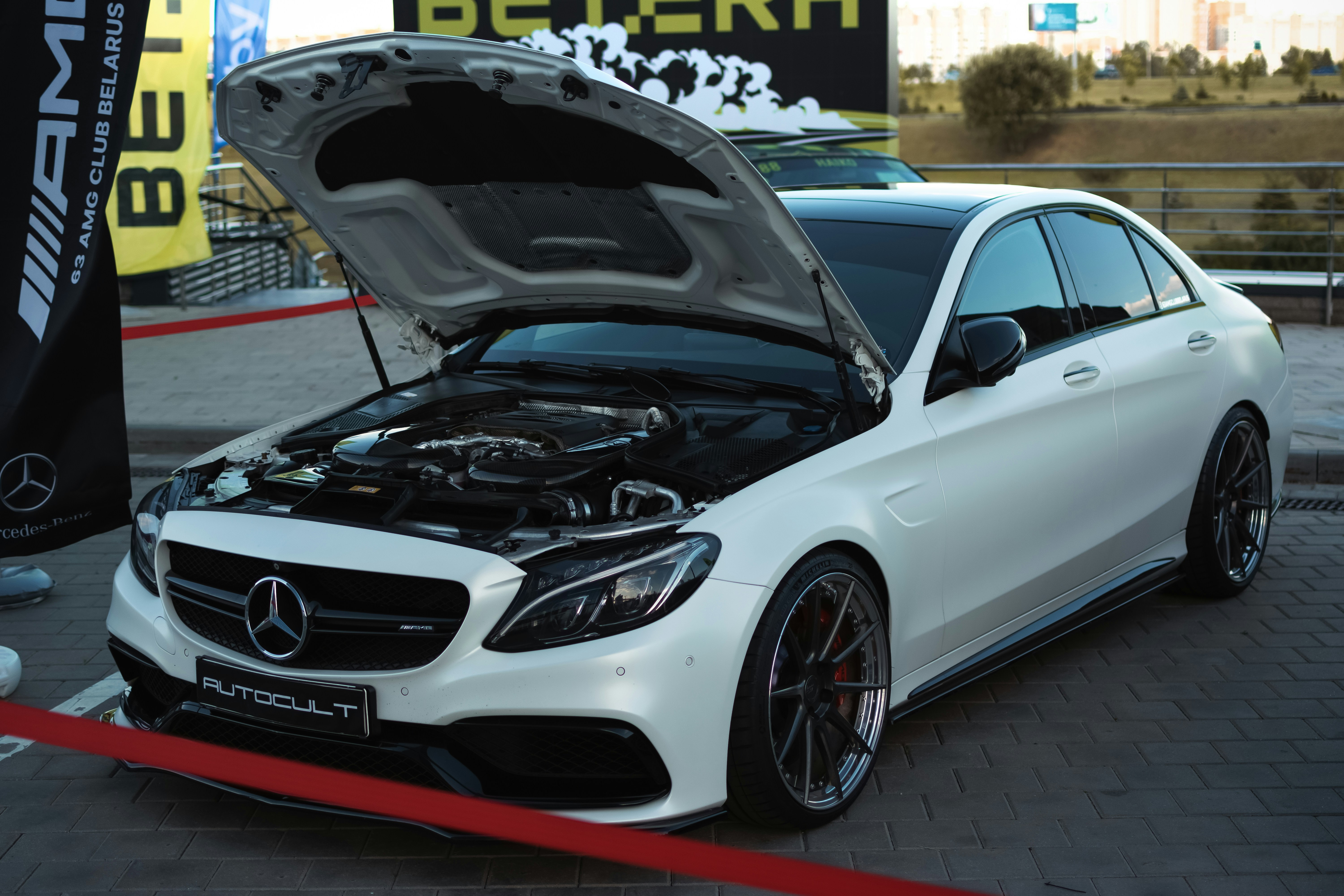 A white car with its hood open parked in a parking lot