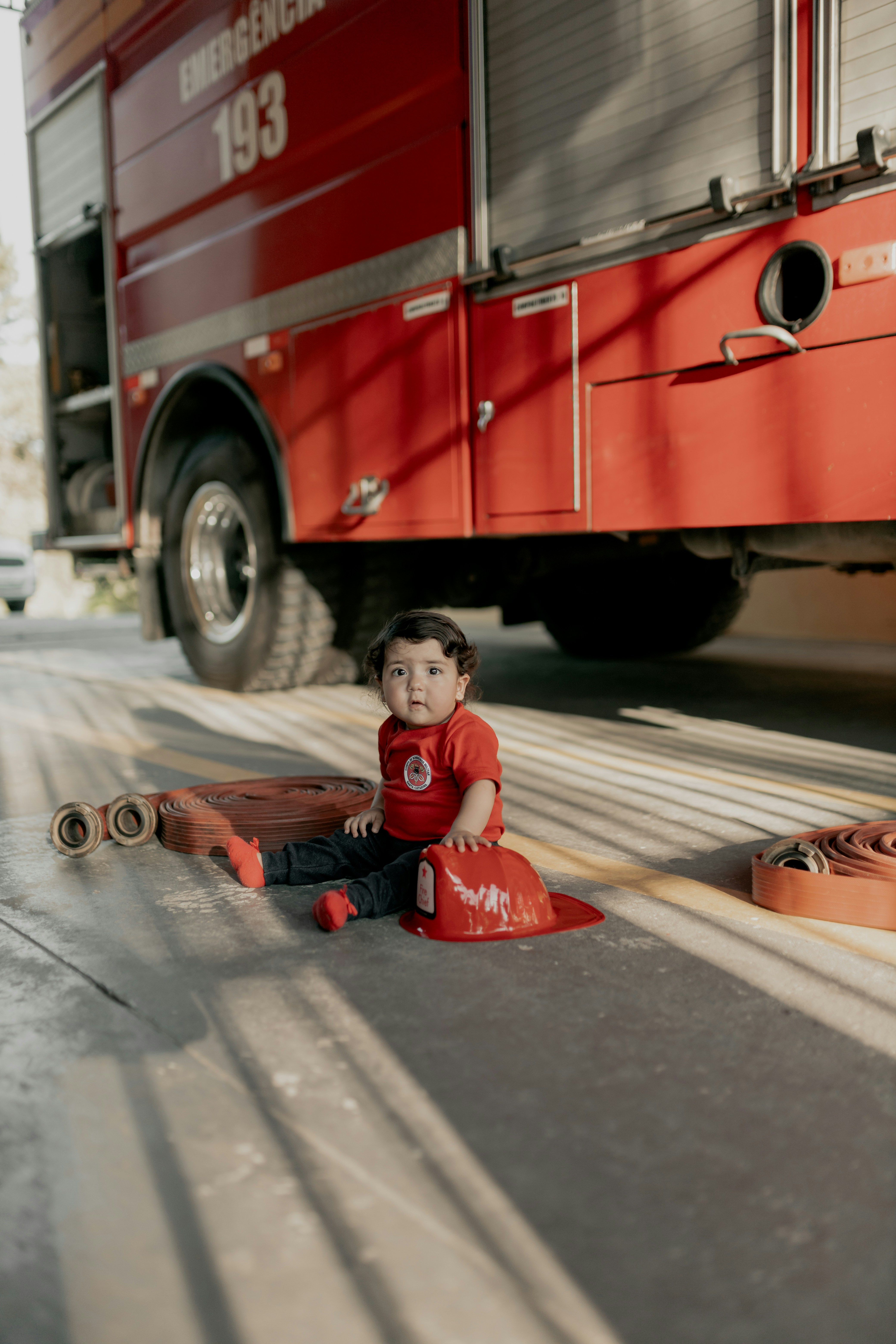 A little boy sitting on the ground in front of a fire truck