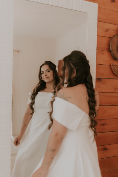 A woman standing in front of a mirror wearing a white dress