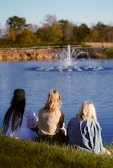 A group of people sitting on the grass near a lake