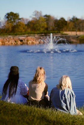 A group of people sitting on the grass near a lake