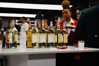 A group of people standing around a table filled with bottles of wine