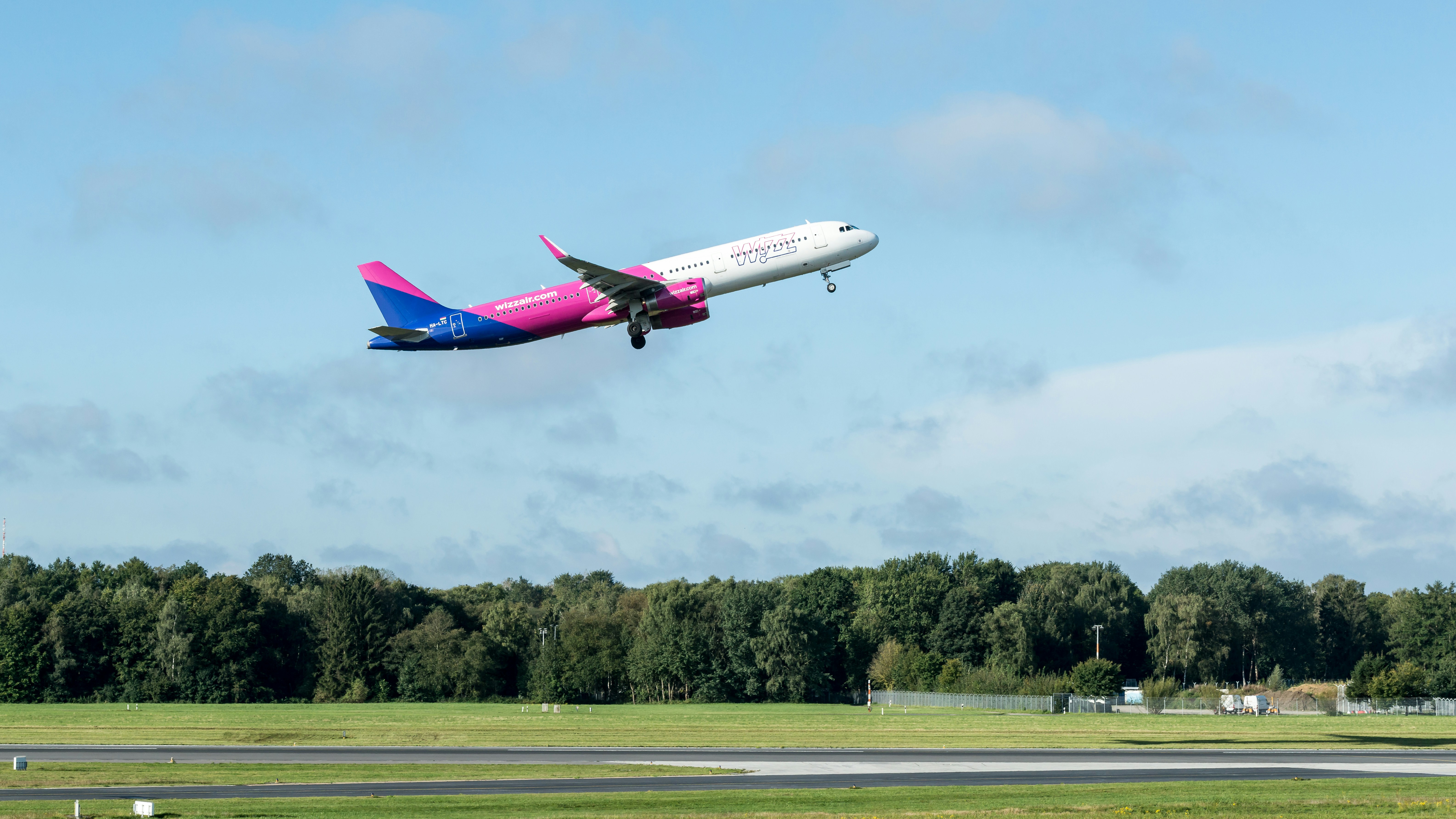 A pink and blue airplane flying over a runway, 