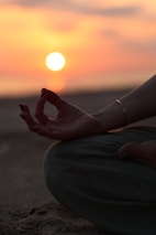 A person sitting in a yoga position with the sun setting in the background