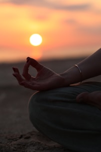 A person sitting in a yoga position with the sun setting in the background