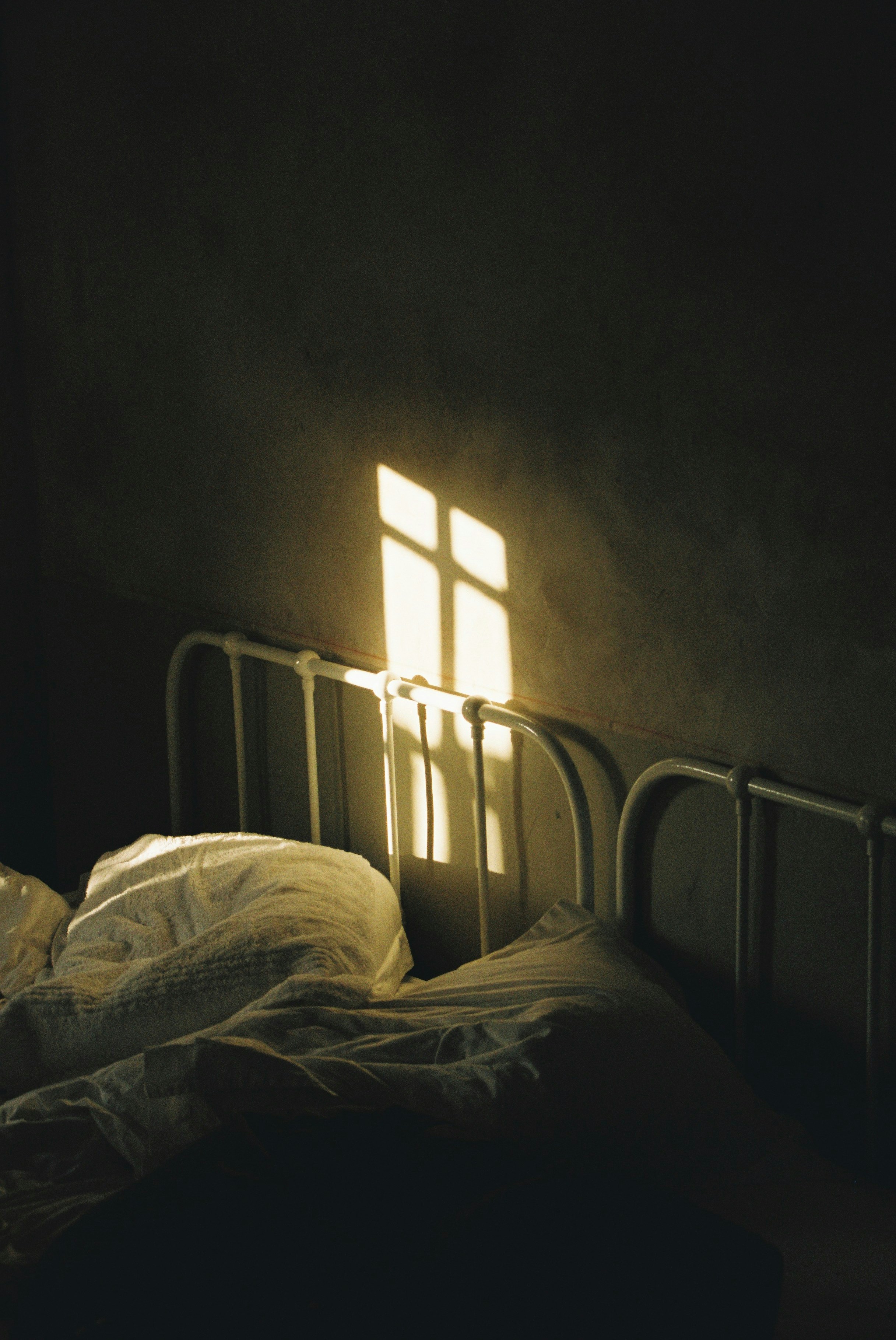 A bed with a light shining through the window