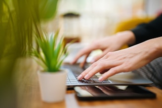 A person typing on a laptop on a wooden table
