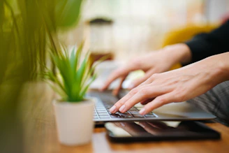 A person typing on a laptop on a wooden table