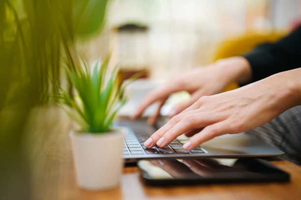 A person typing on a laptop on a wooden table