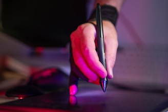 A person holding a pen and writing on a laptop