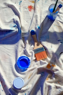 A table topped with paint and brushes on top of a white cloth