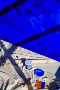 A blue tarp with paint and brushes on it