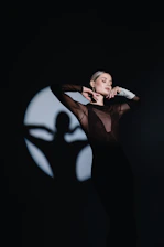 A woman standing in the dark with her arms behind her head
