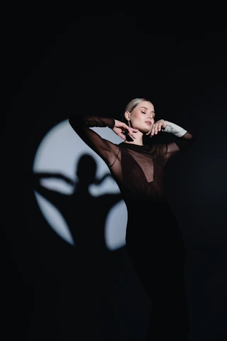 A woman standing in the dark with her arms behind her head