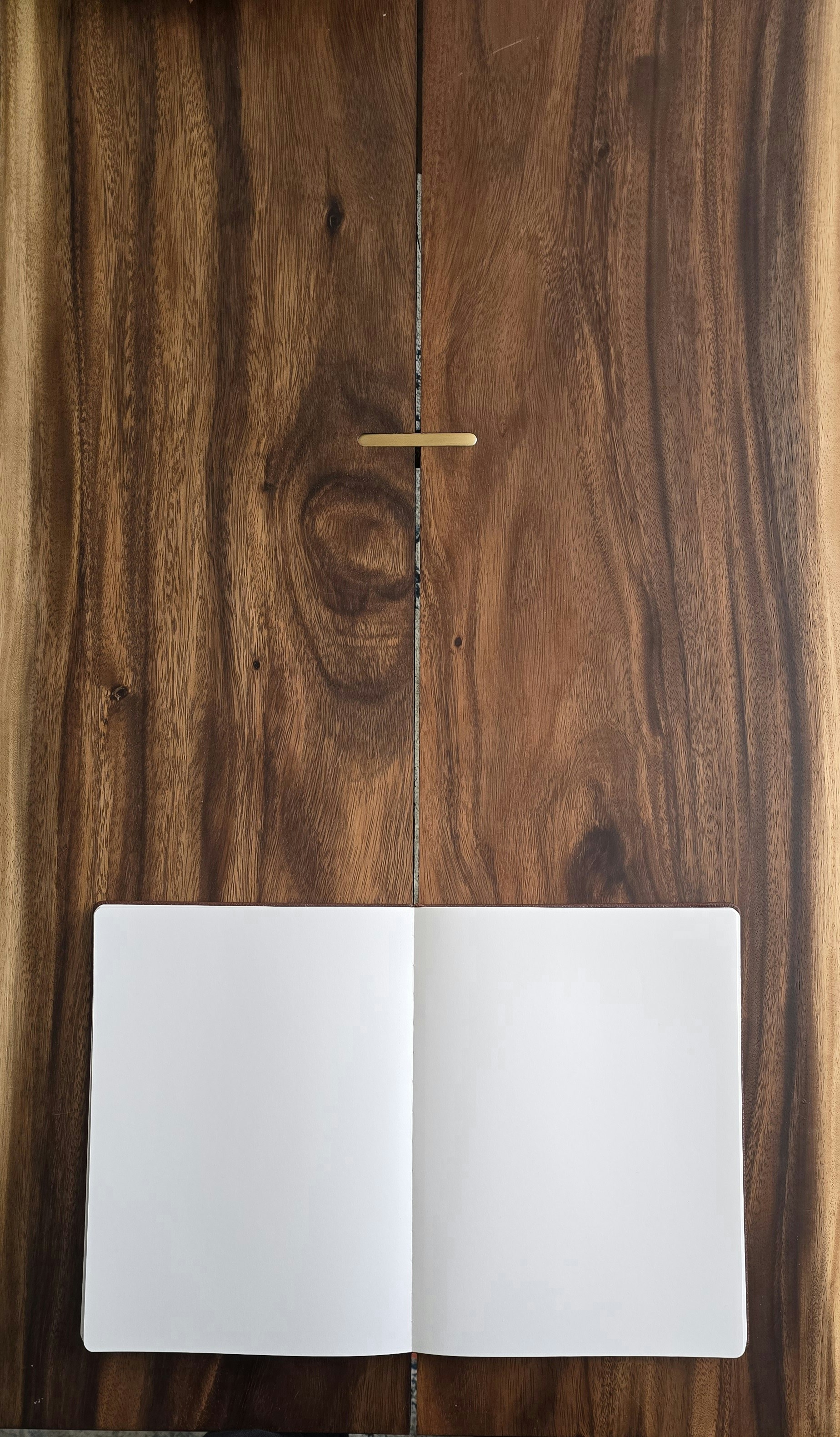 Cuaderno abierto con páginas en blanco sobre superficie de madera cálida, luz natural suave