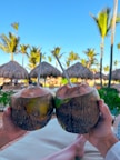 A person holding two coconuts in front of a beach