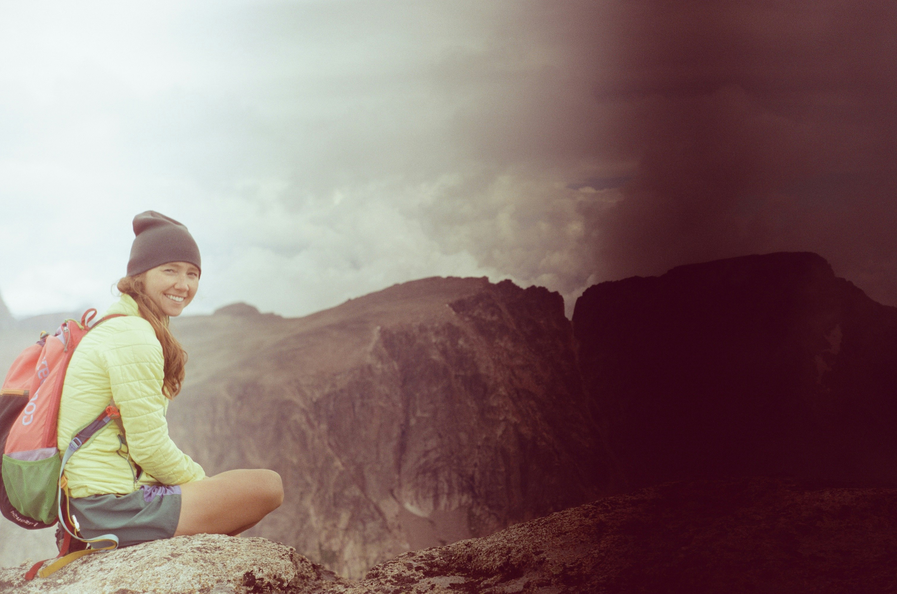 A woman sitting on top of a mountain with a backpack