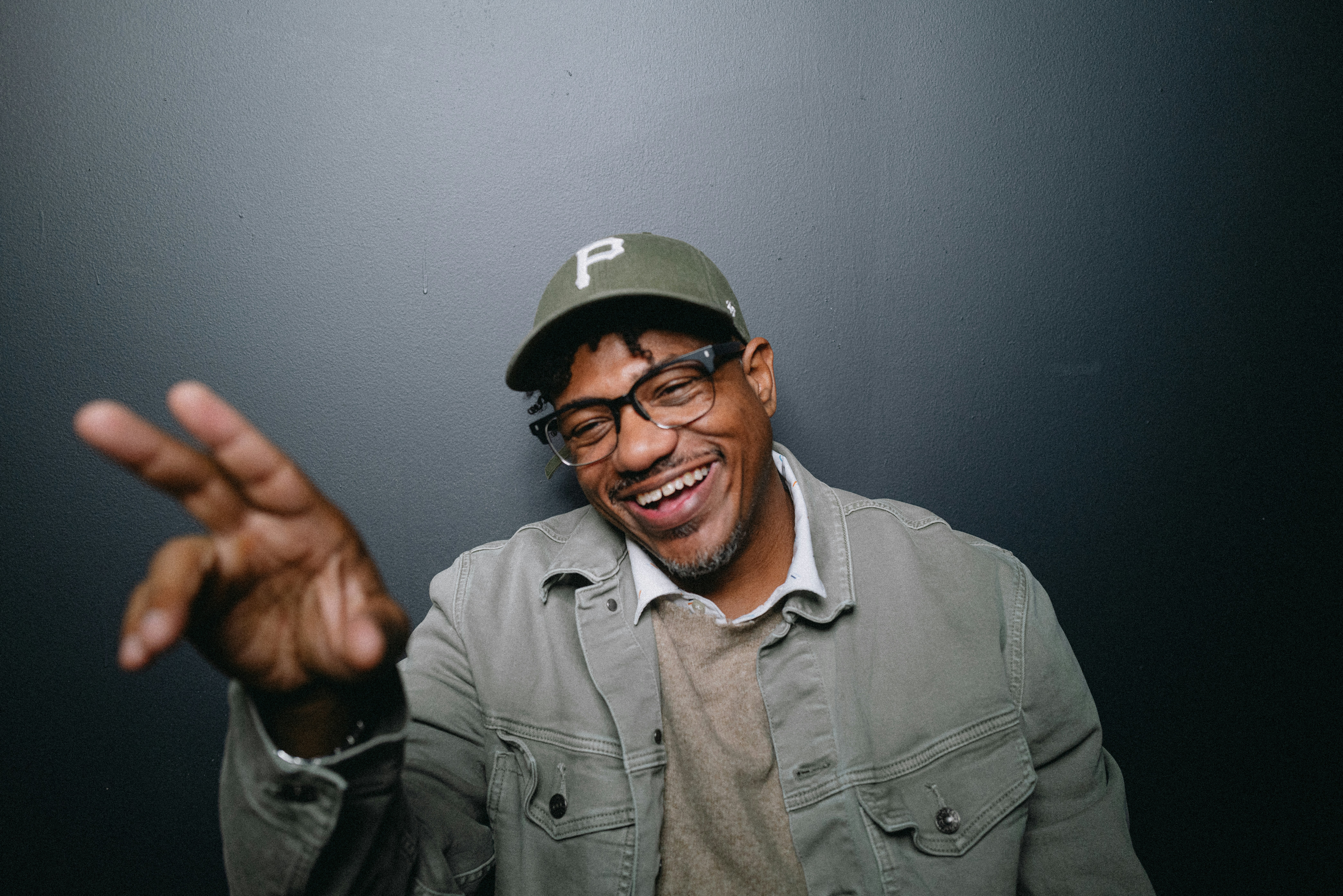 A man wearing a hat and glasses making a hand gesture