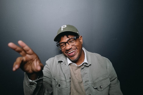 A man wearing a hat and glasses making a hand gesture