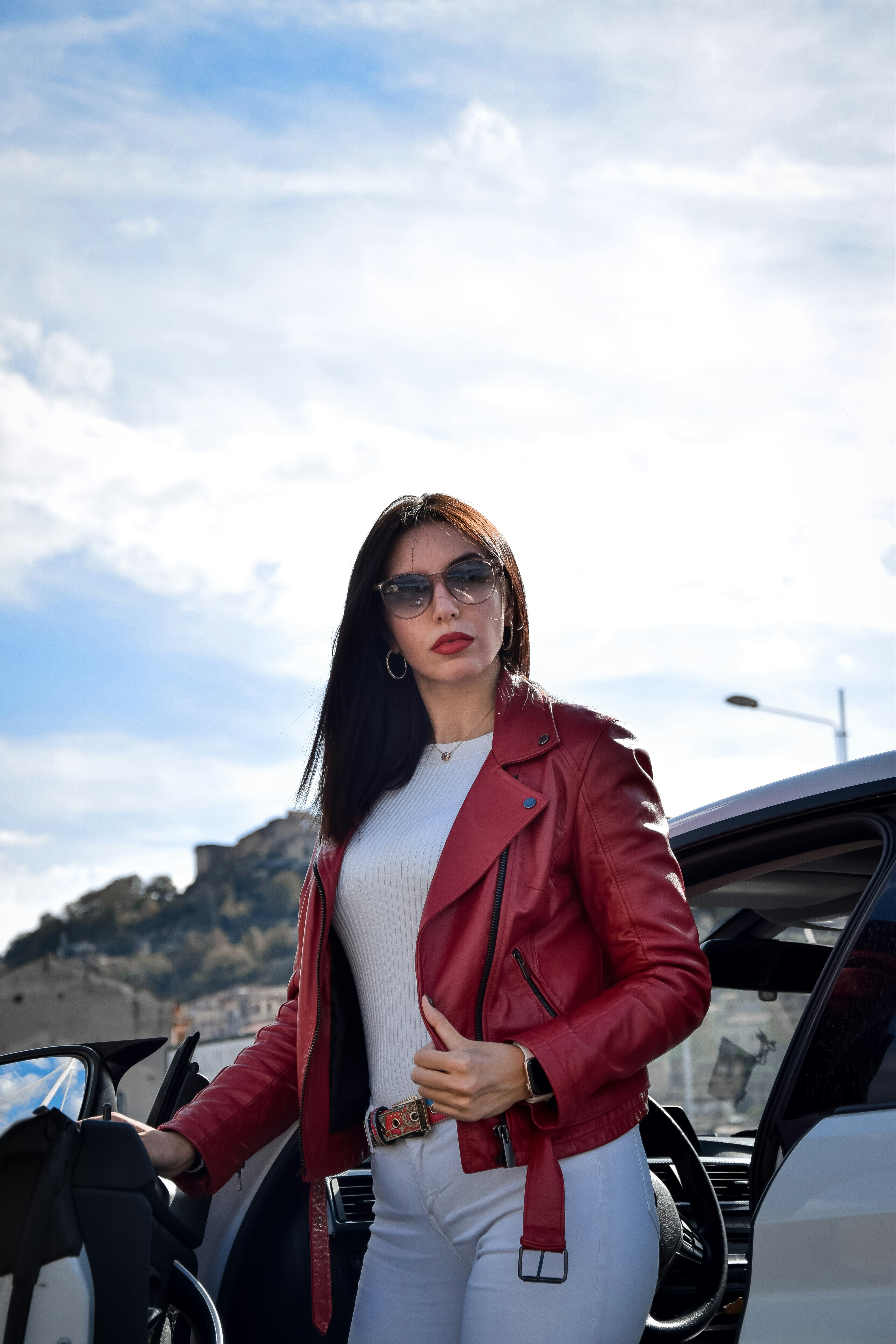 This image captures a bold and confident style statement. The woman, dressed in a striking red leather jacket over a crisp white outfit, is complemented by a pair of sleek, gradient-tinted sunglasses. These sunglasses not only enhance her modern and edgy look but also offer a perfect blend of fashion and functionality.