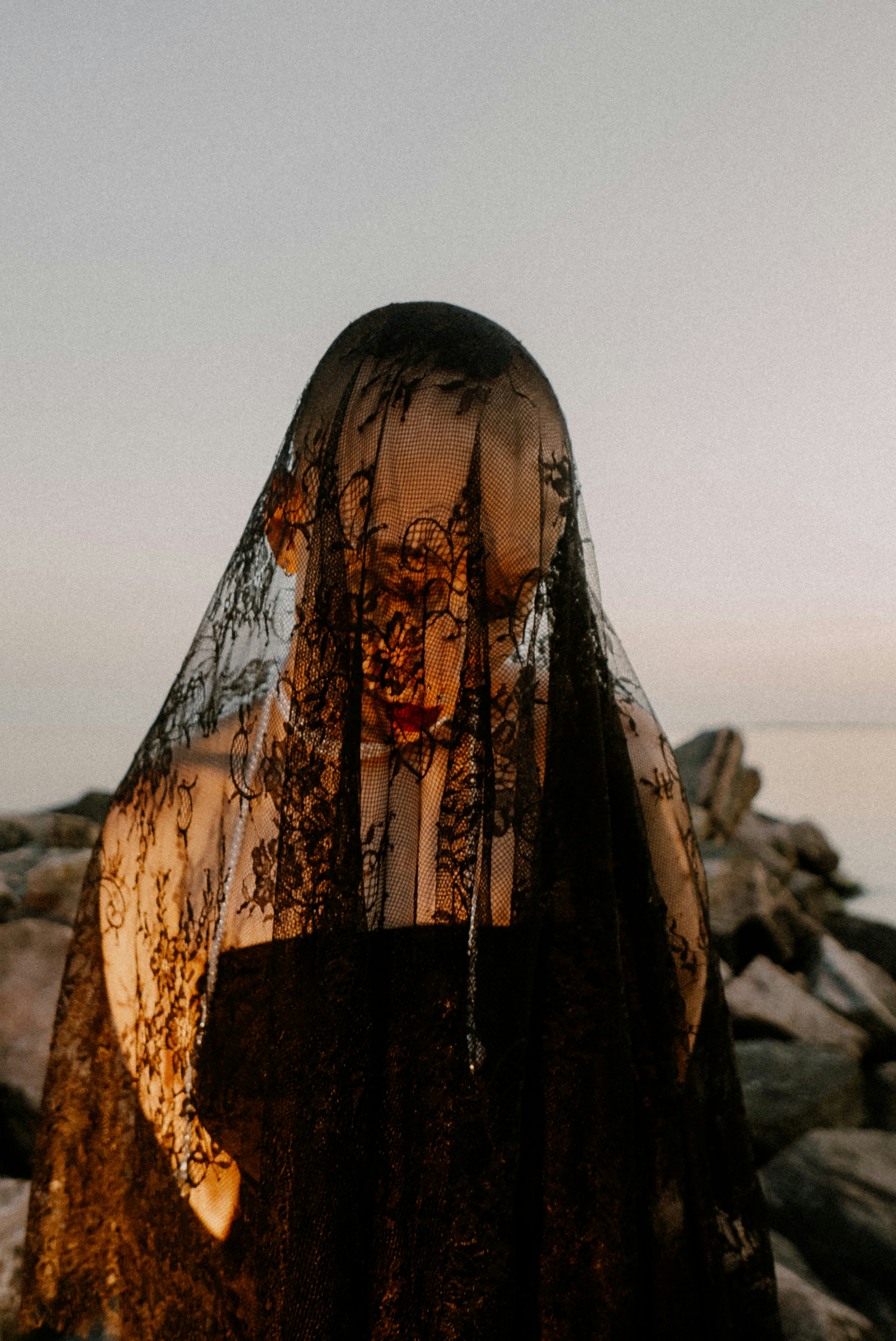 A woman wearing a veil standing on a rocky beach