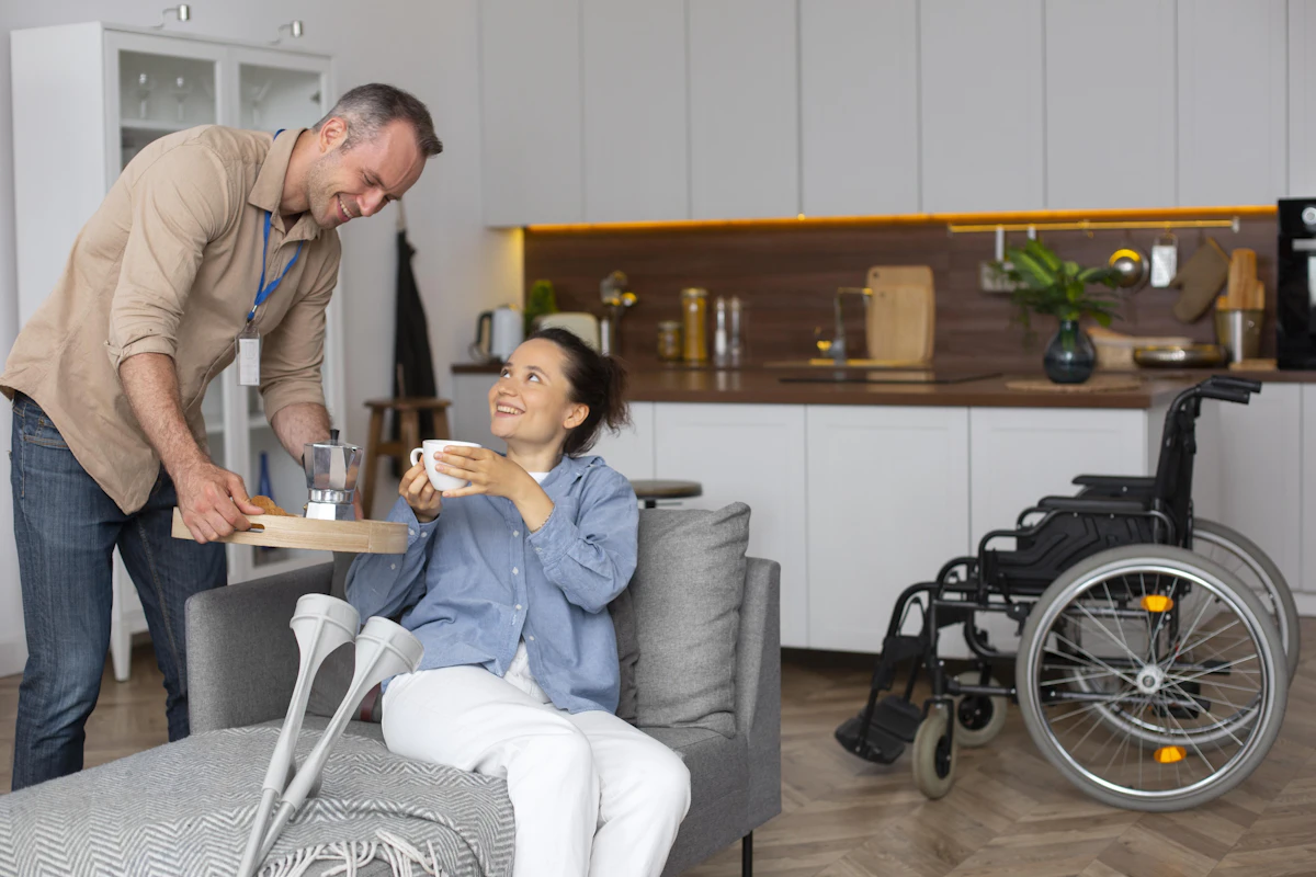 A support worker bringing a cup of tea to a woman relaxing at home, her wheelchair nearby