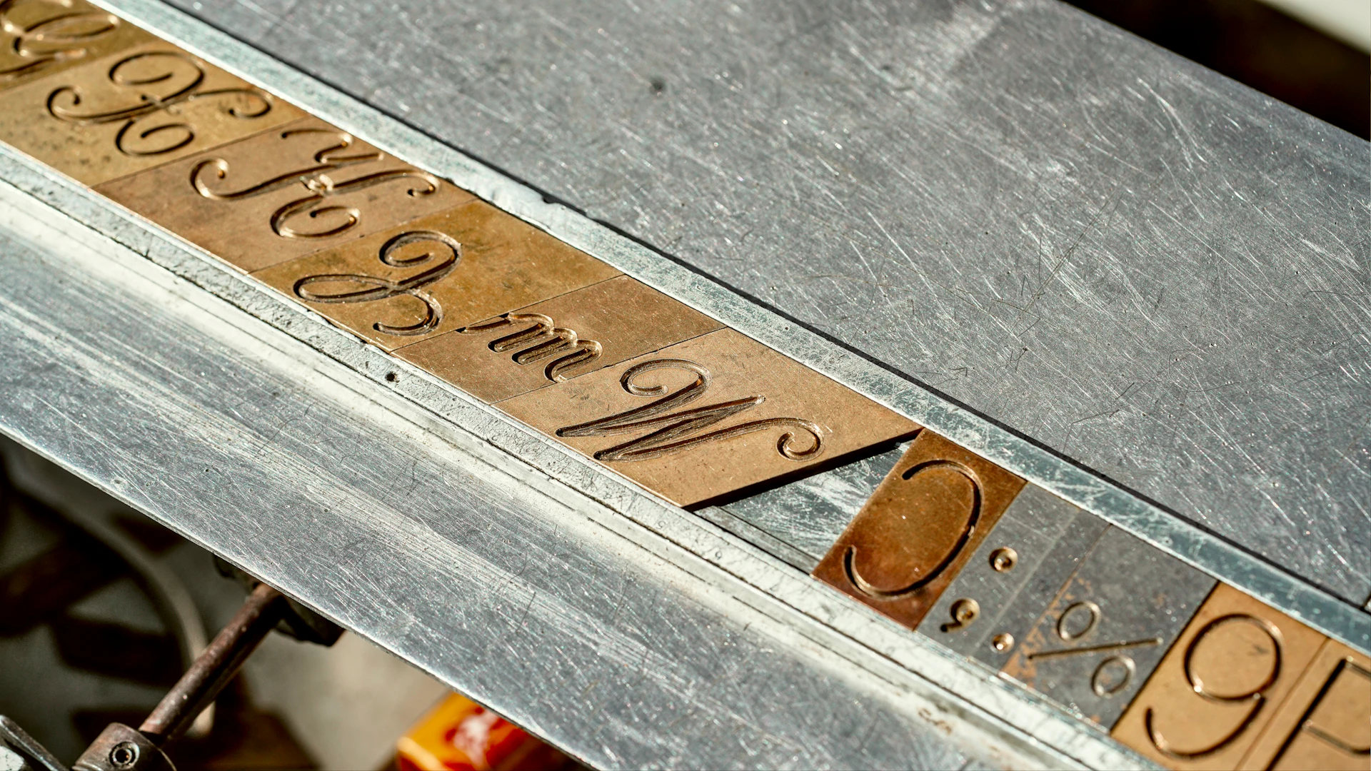 Brass letter templates on an engraving machine bed, used to trace lettering onto metal