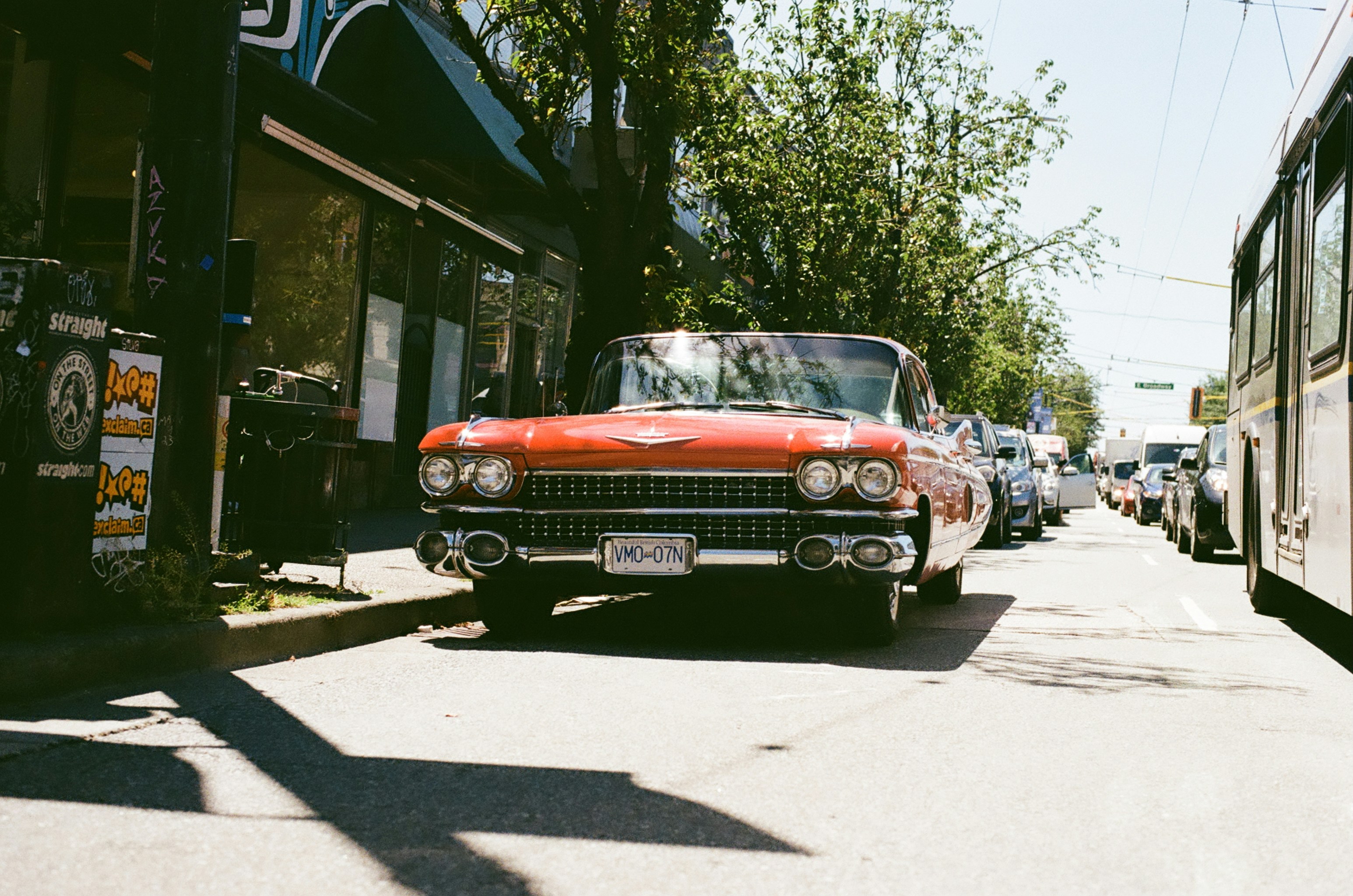 A red car driving down a street next to a bus