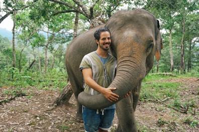 A man standing next to an elephant in a forest