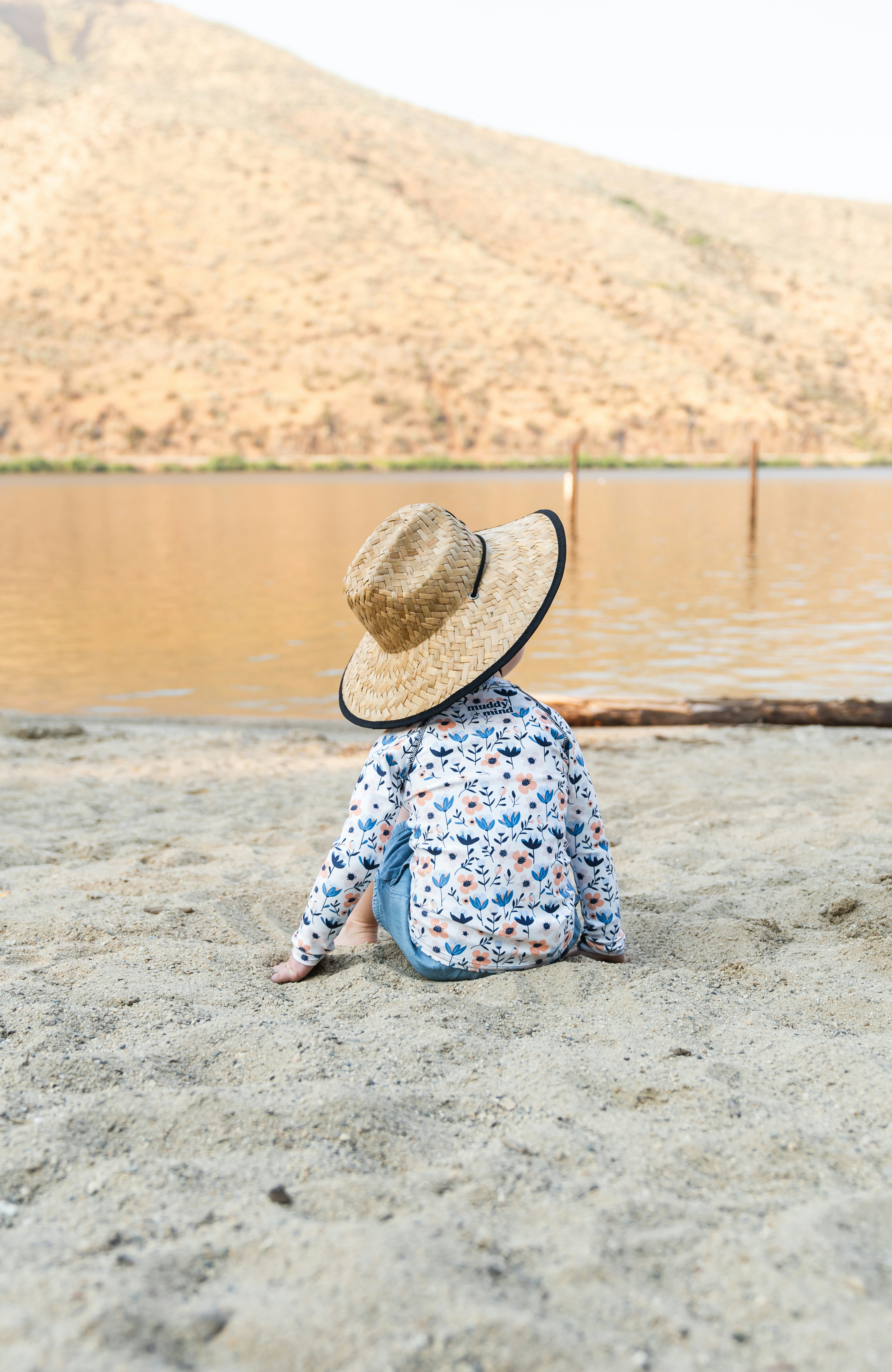 A little girl sitting on the beach wearing a hat