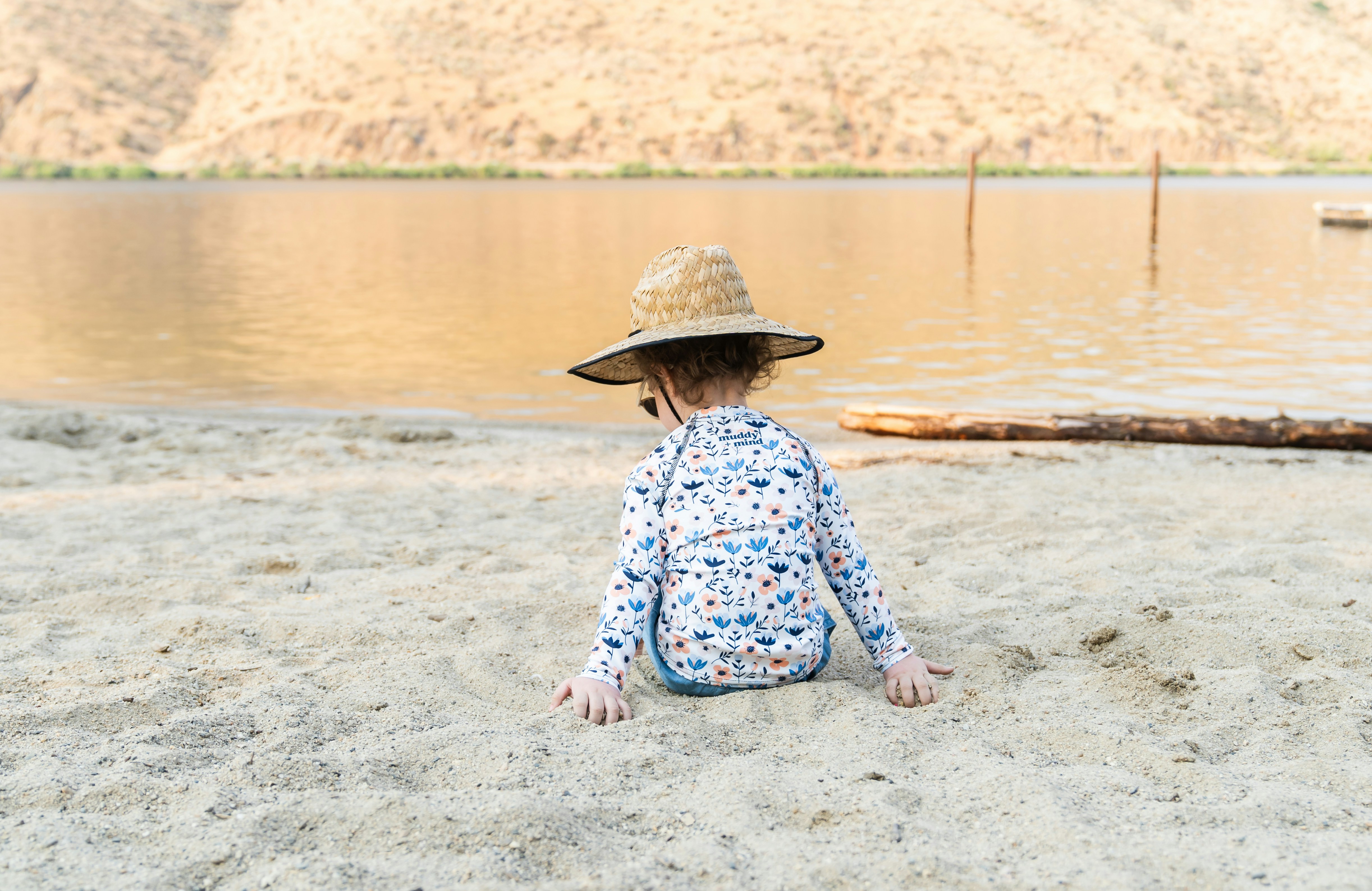 A little girl sitting on the beach wearing a hat