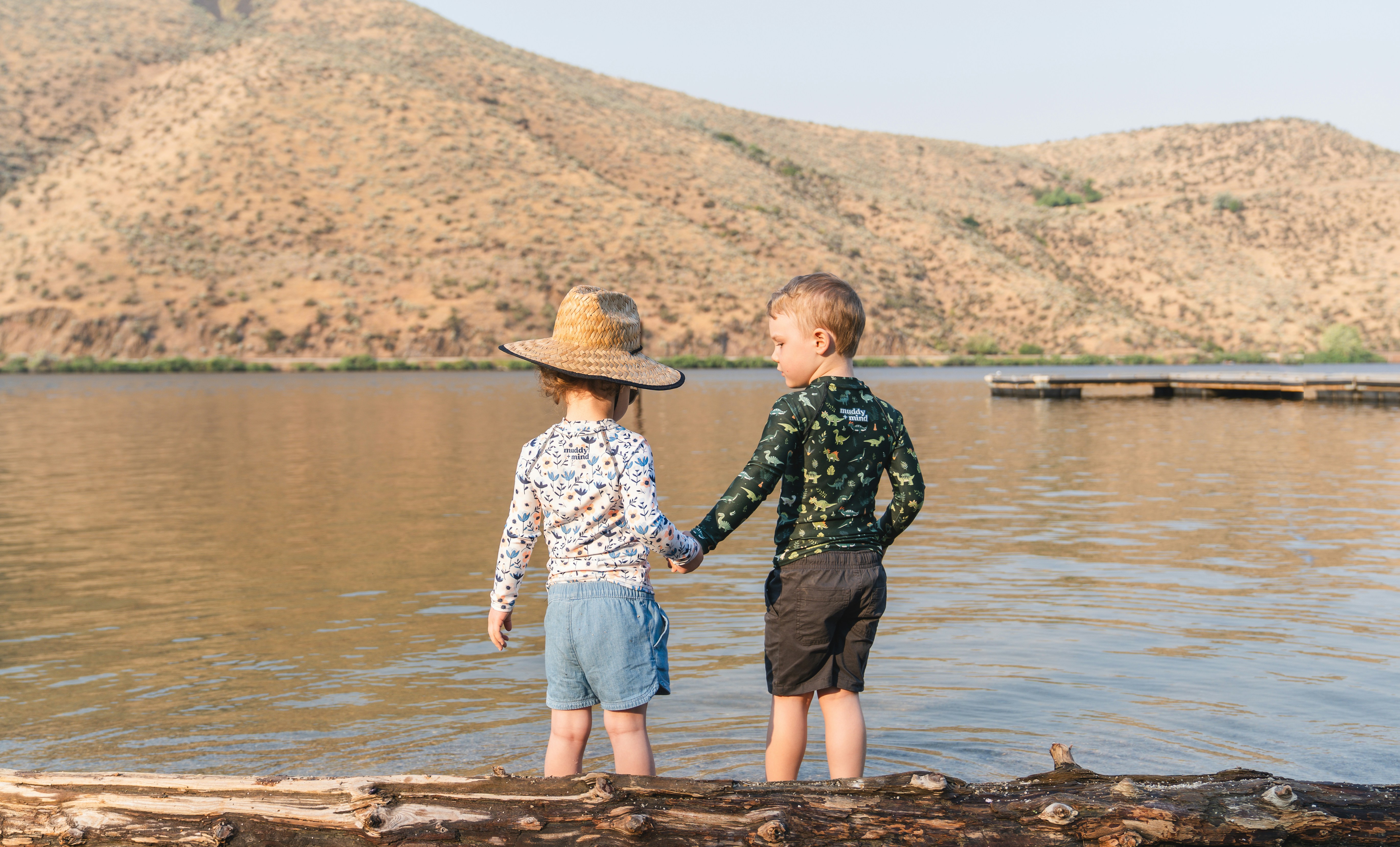 Two young boys standing on a log by the water