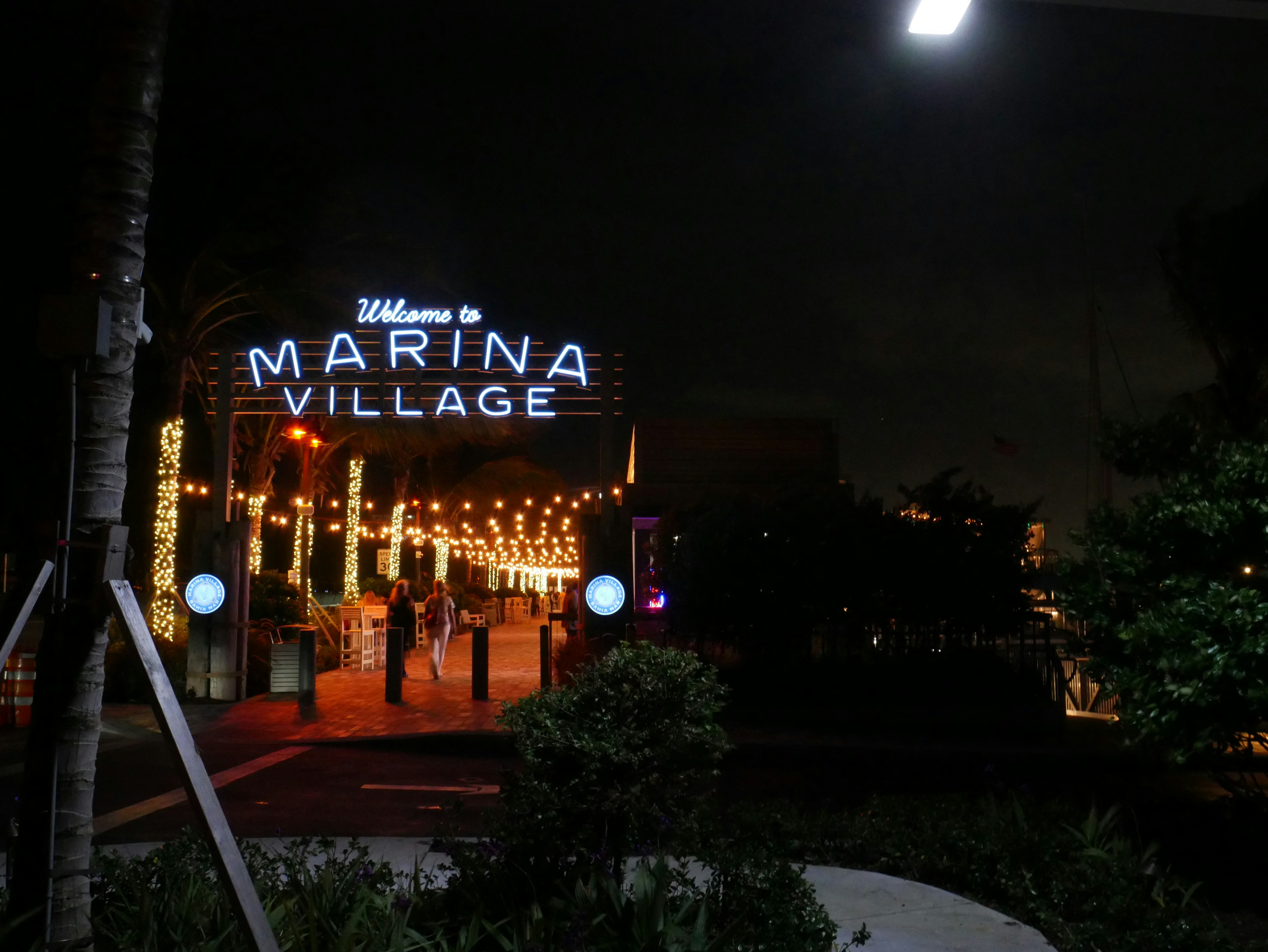 A sign that reads marina village lit up at night