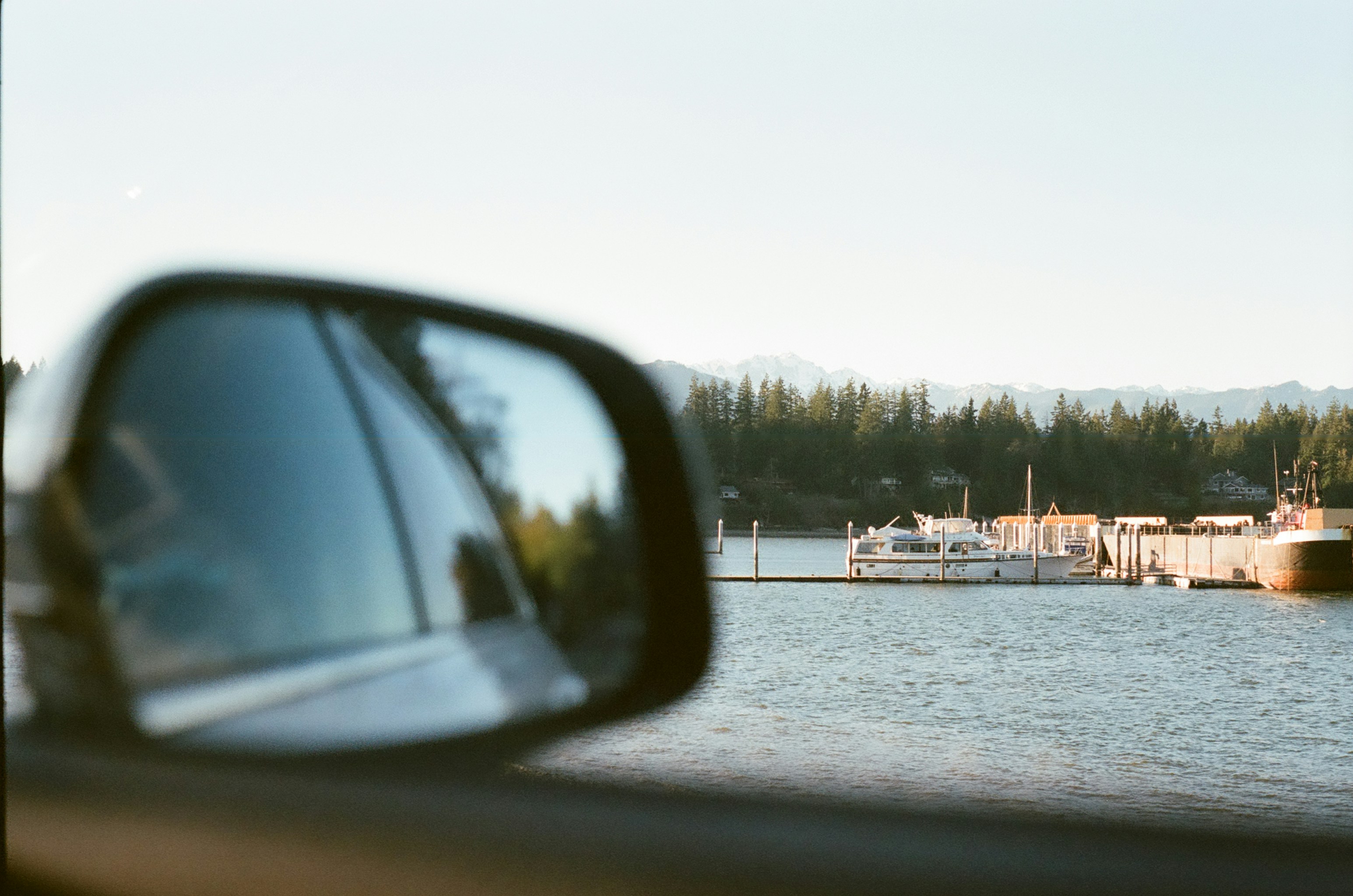A car's side view mirror reflecting boats in the water