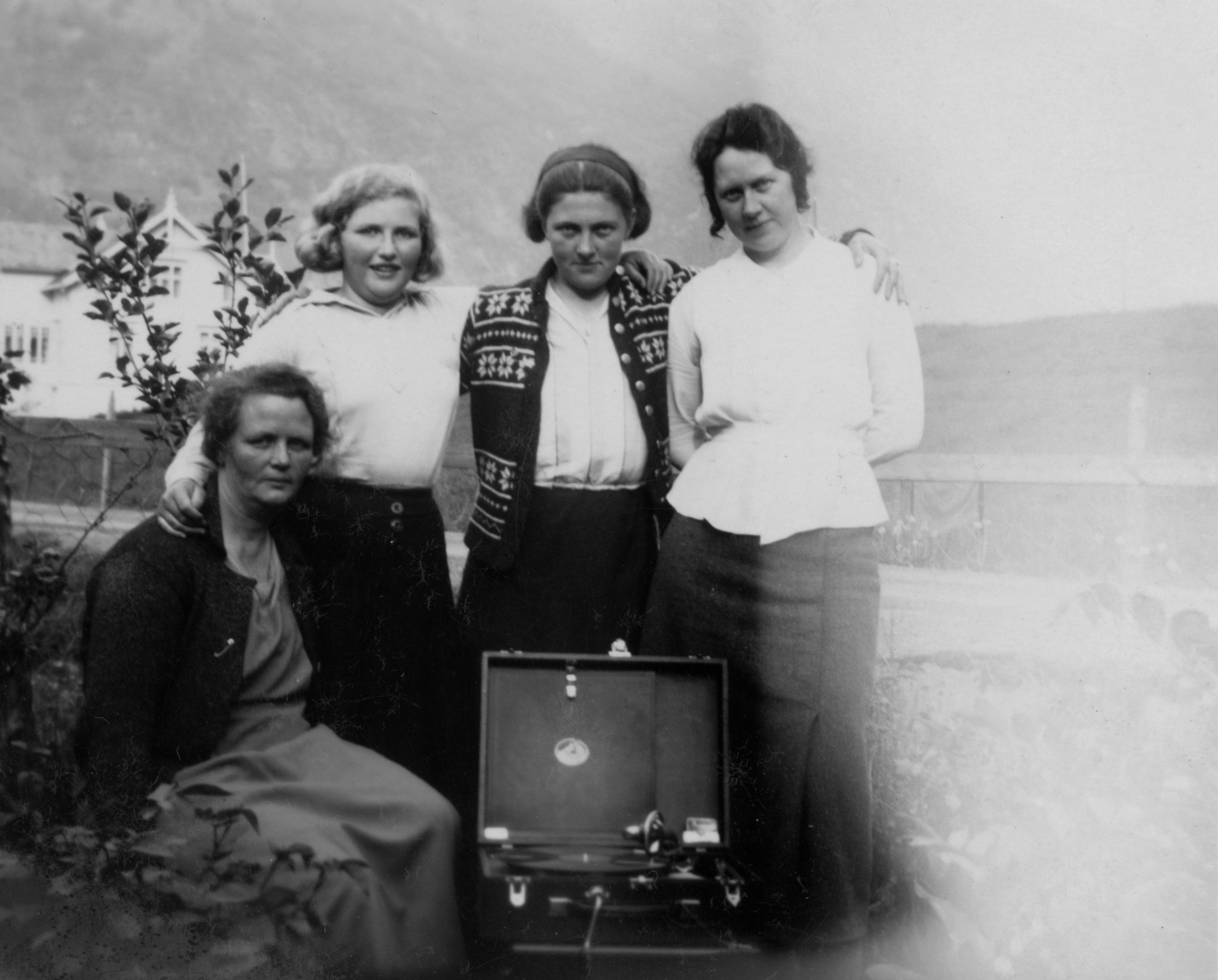 Four women pose with a record player outdoors.