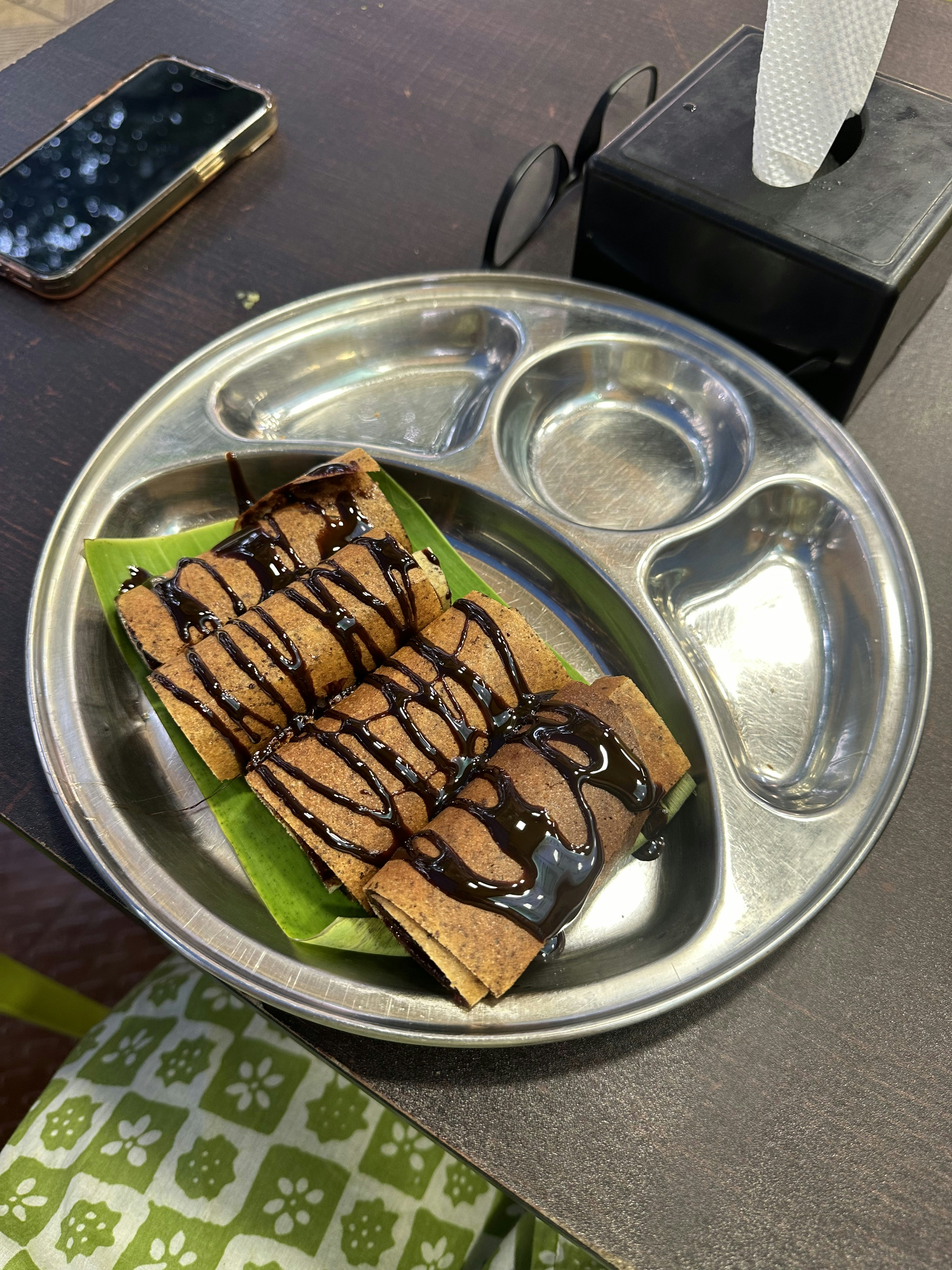 Rolled chocolate crepes drizzled with ganache sauce on dark stone surface, dim warm restaurant lighting
