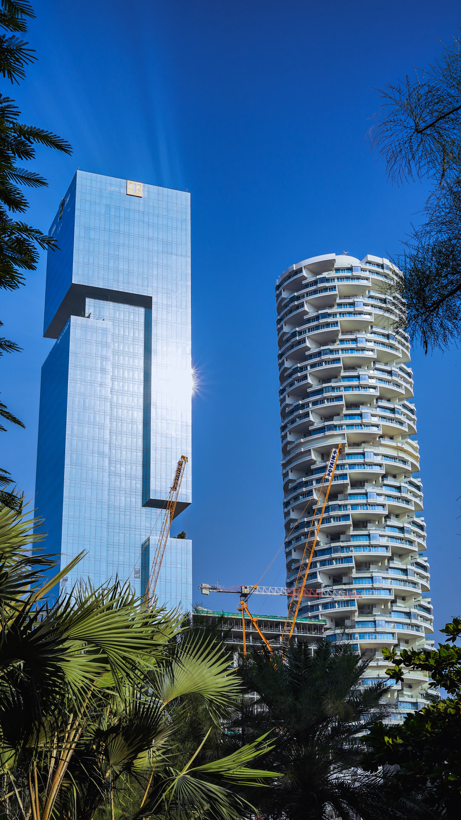 The round FIVE Jumeirah Village tower with stacked balconies beside a notched glass high-rise in the developing JVC district of Dubai.